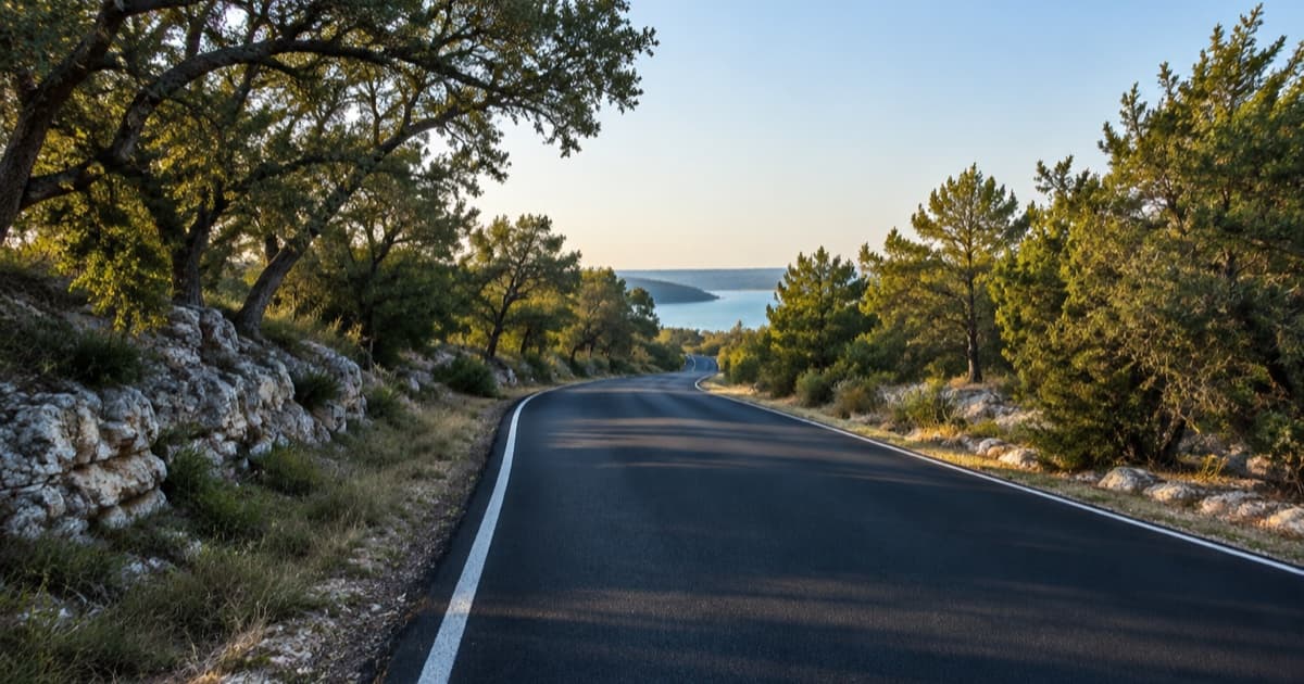 A newly paved two-lane road curving past limestone and oak trees toward a lake in the Texas Hill Country. AI illustration, not a real Lago Vista street.